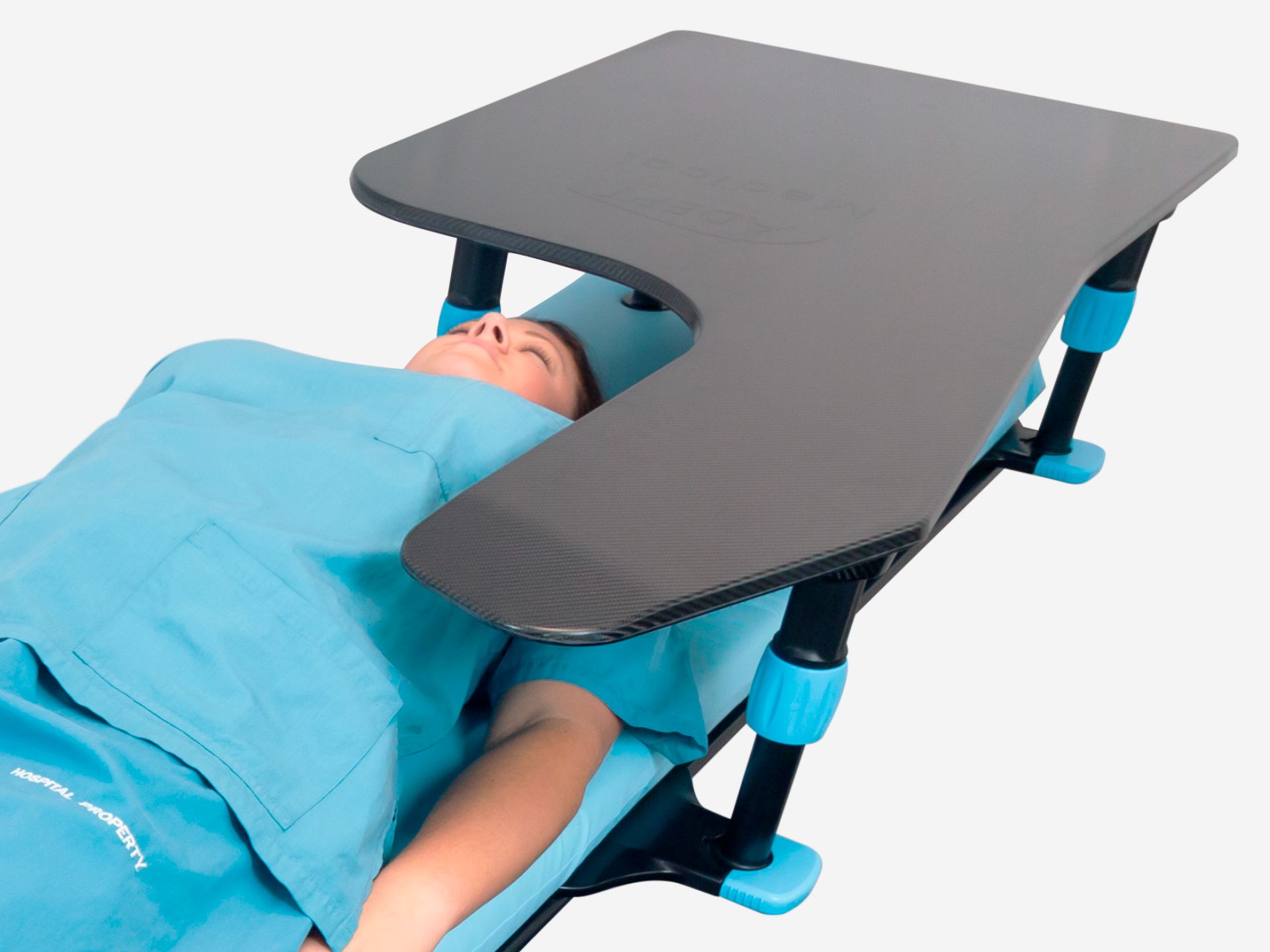 A person in blue scrubs lies under a dark gray U-shaped medical table with blue accents.