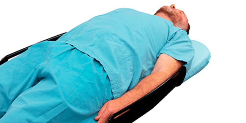 A man in teal scrubs lying on his back on a stretcher.