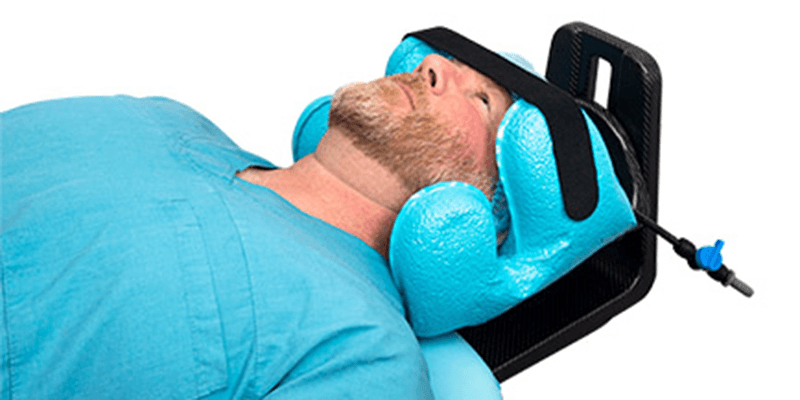 Head of a man in blue scrubs, resting in a light blue medical head support system.