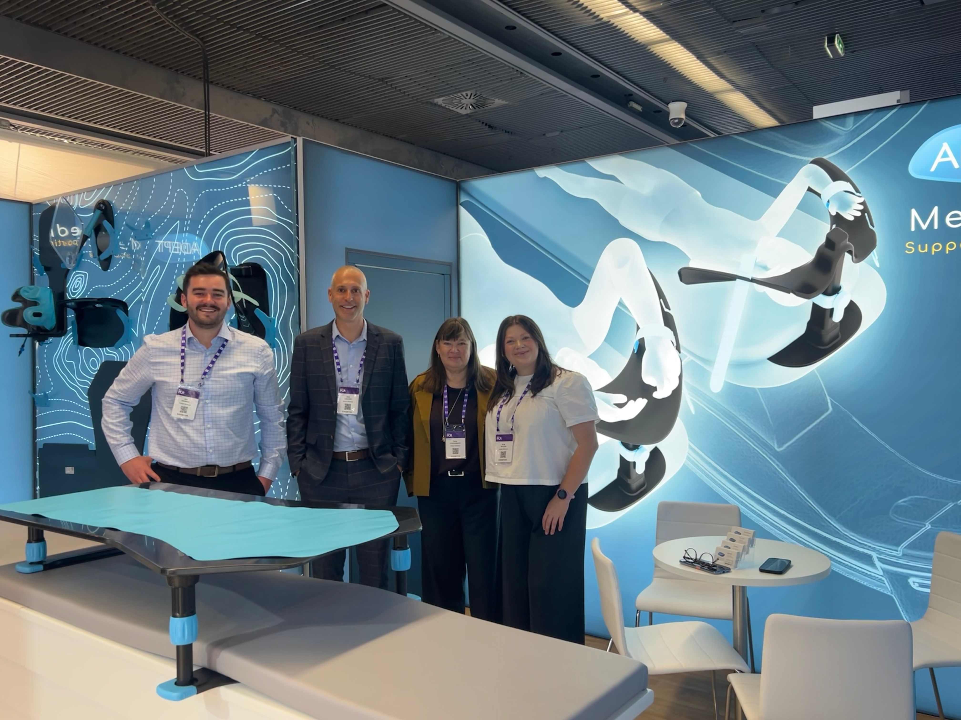 Two men and two women smiling in a trade show booth with product displays.