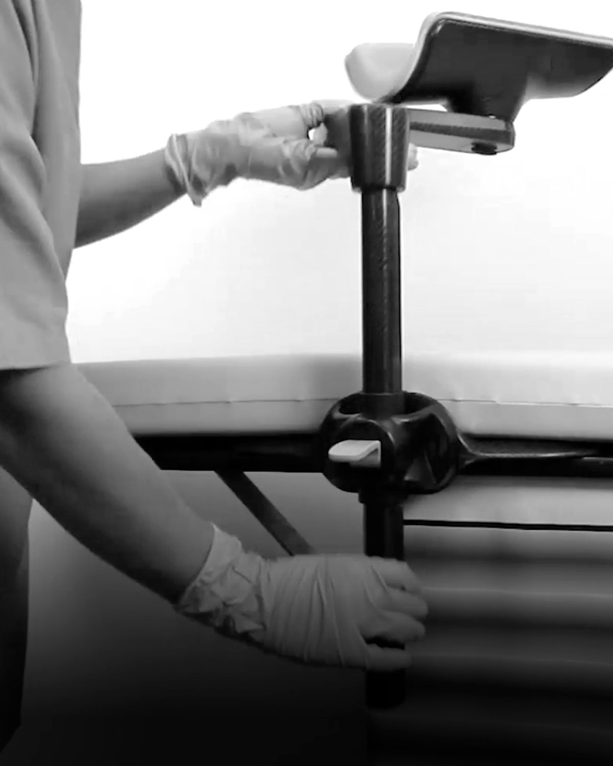Gloved hands adjusting a medical arm support clamped to a treatment table.