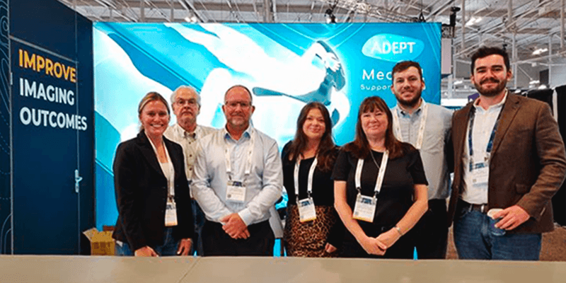 Seven people pose in front of an ADEPT Medical Support trade show booth.
