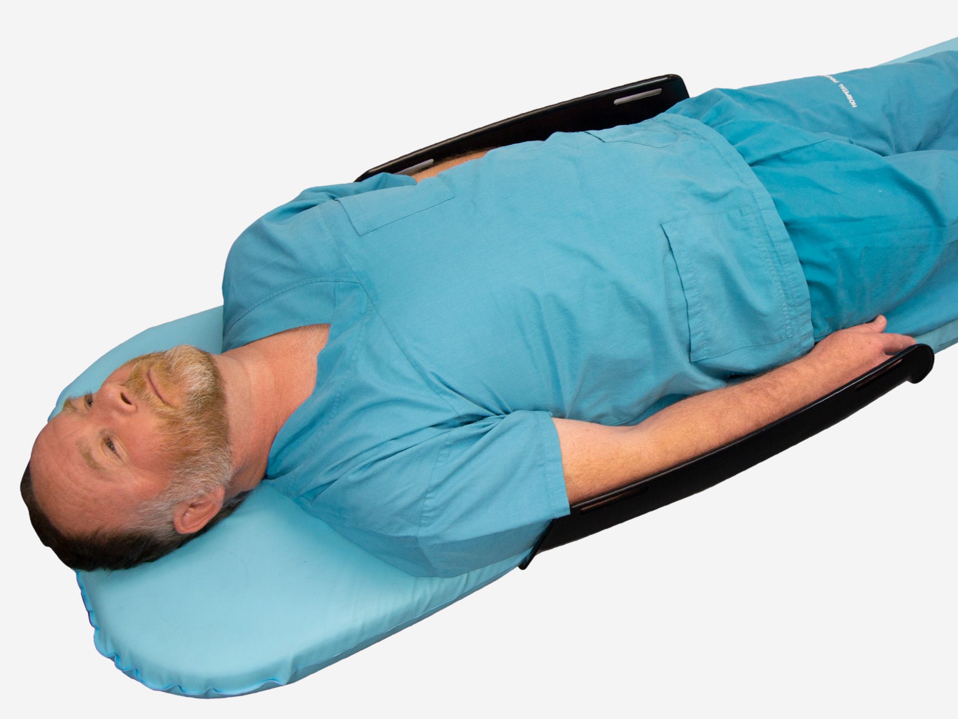 Man in blue scrubs lying supine on a medical table with a blue headrest and black arm supports.