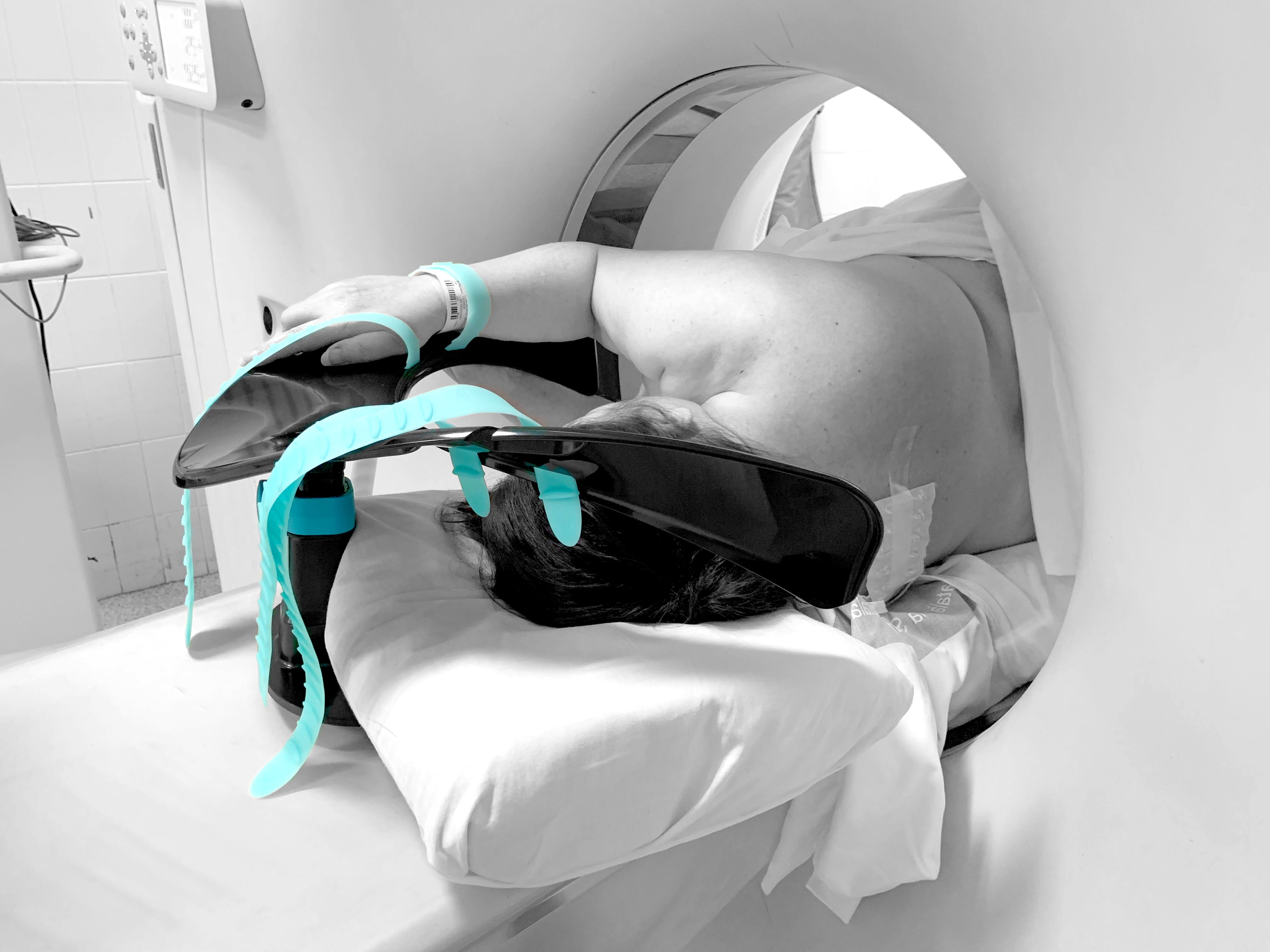 A person lying face down with arms extended on a teal and black support device, partially inside a medical scanner.