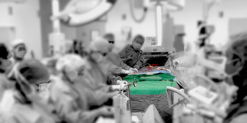 Surgeons operating on a patient, with the surgical field visible in color against a desaturated, blurry background.